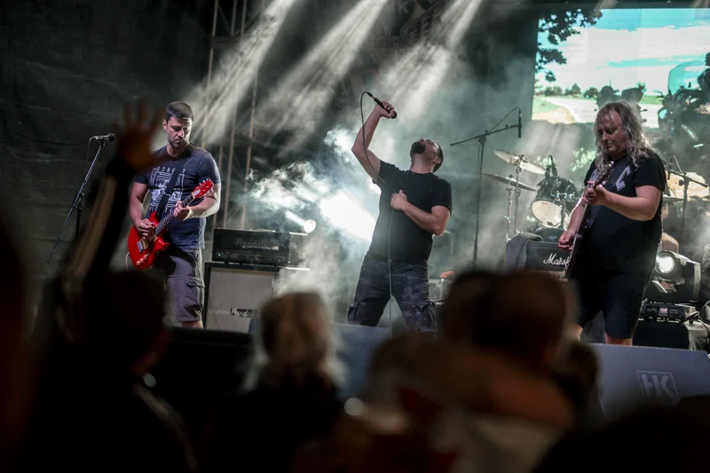 Penampilan band rock di panggung festival musik outdoor dengan sorotan tata lampu dramatis, tata suara gantung, dan struktur rigging kokoh
